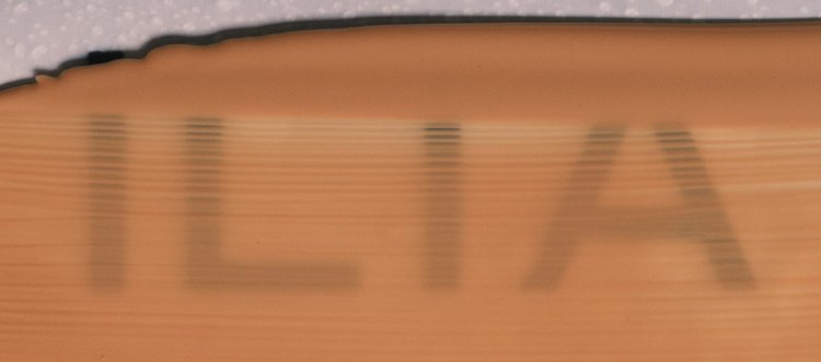 Close-up van ILIA Skin Tint uitgestreken over een flesje, met het ILIA-logo zichtbaar door de vloeistof