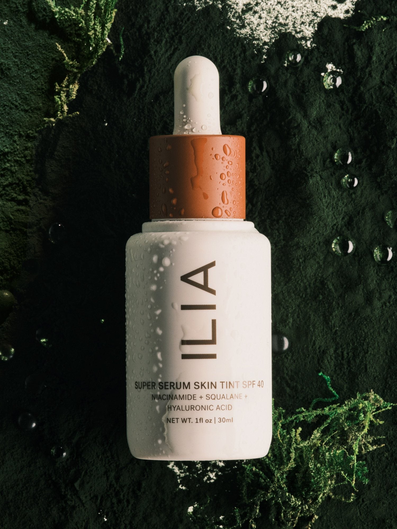 Super Serum Skin Tint SPF 40 op donkergroen mos met waterdruppels